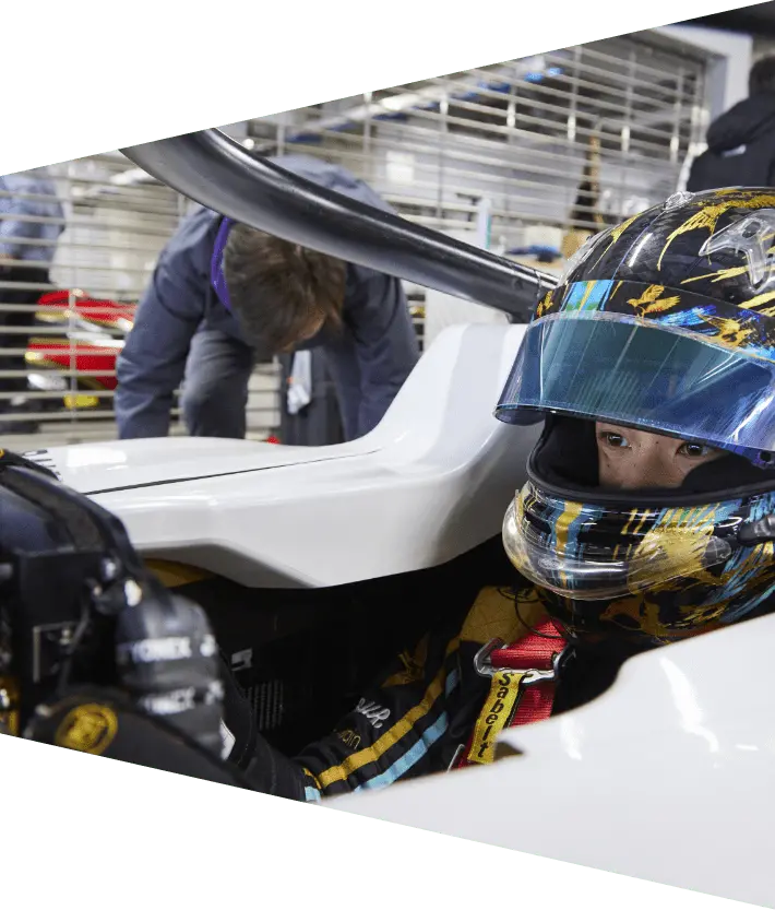 レーシングヘルメットをかぶったドライバーがコックピットに座り、走行準備をしている様子